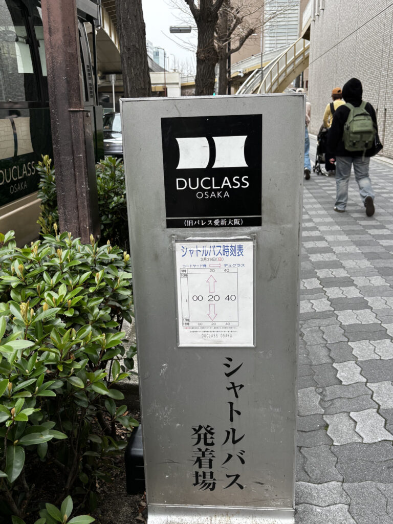 新大阪駅2番出口前のシャトルバス乗り場に設置された、デュクラス大阪のロゴ入り案内看板(運行スケジュールと停車位置の表示)